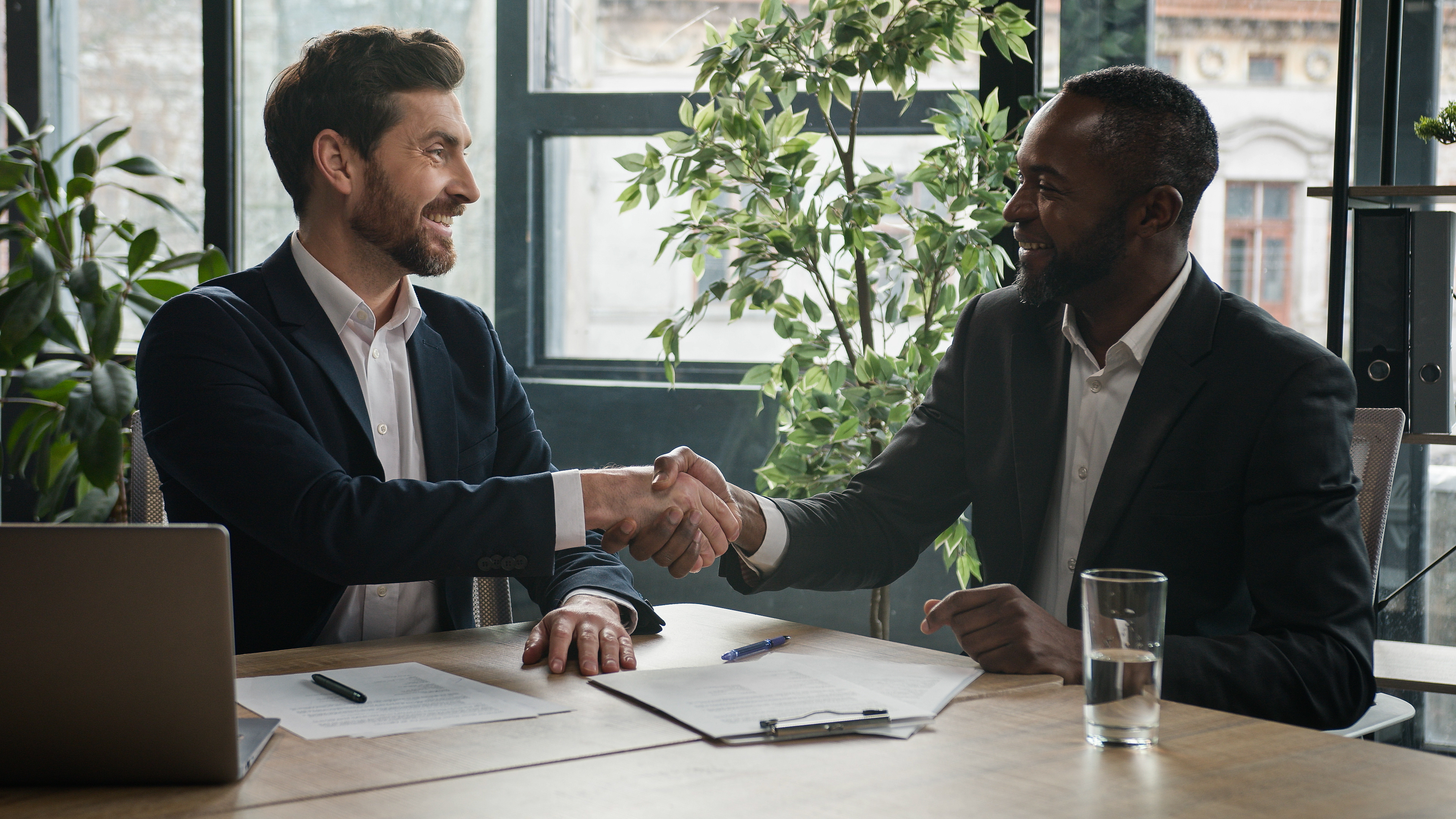 Two businessmen smiling and shaking hands across a desk